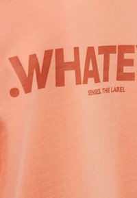 Peach cotton t-shirt featuring bold brown text that reads ".WHATEVER SENSES. THE LABEL" centered on the chest. Smooth texture.