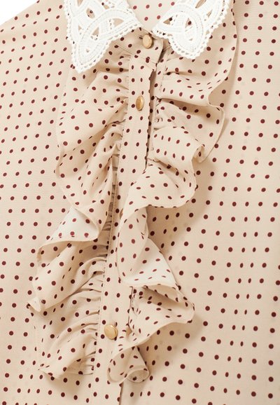Beige blouse met bordeauxrode stippen, met een gerimpelde voorkant, gouden knopen en een kanten kraag. Zachte stof met een delicate textuur.