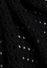 Schwarzer Strickstoff mit einem strukturierten, Durchbruchs-Muster, durch das der weiße Hintergrund durch die Löcher sichtbar ist.