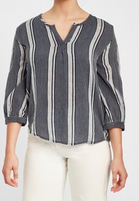 Bluzka w paski w kolorze granatowym i białym, wykonana z lekkiego materiału, z dekoltem w serek, rękawami o długości trzech ćwiartek i lekko zaokrąglonym dołem.