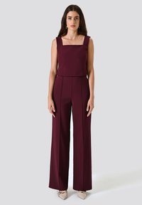 Bordeaux jumpsuit met wijde benen, vierkante halslijn en gestructureerde buste. Gemaakt van een soepel materiaal, met een minimalistisch ontwerp en een getailleerde pasvorm.