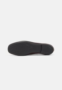 Semelle de chaussure en caoutchouc noir avec des motifs de grip texturés, des rainures ovales et un bout rond. Talon légèrement surélevé et bords lisses.