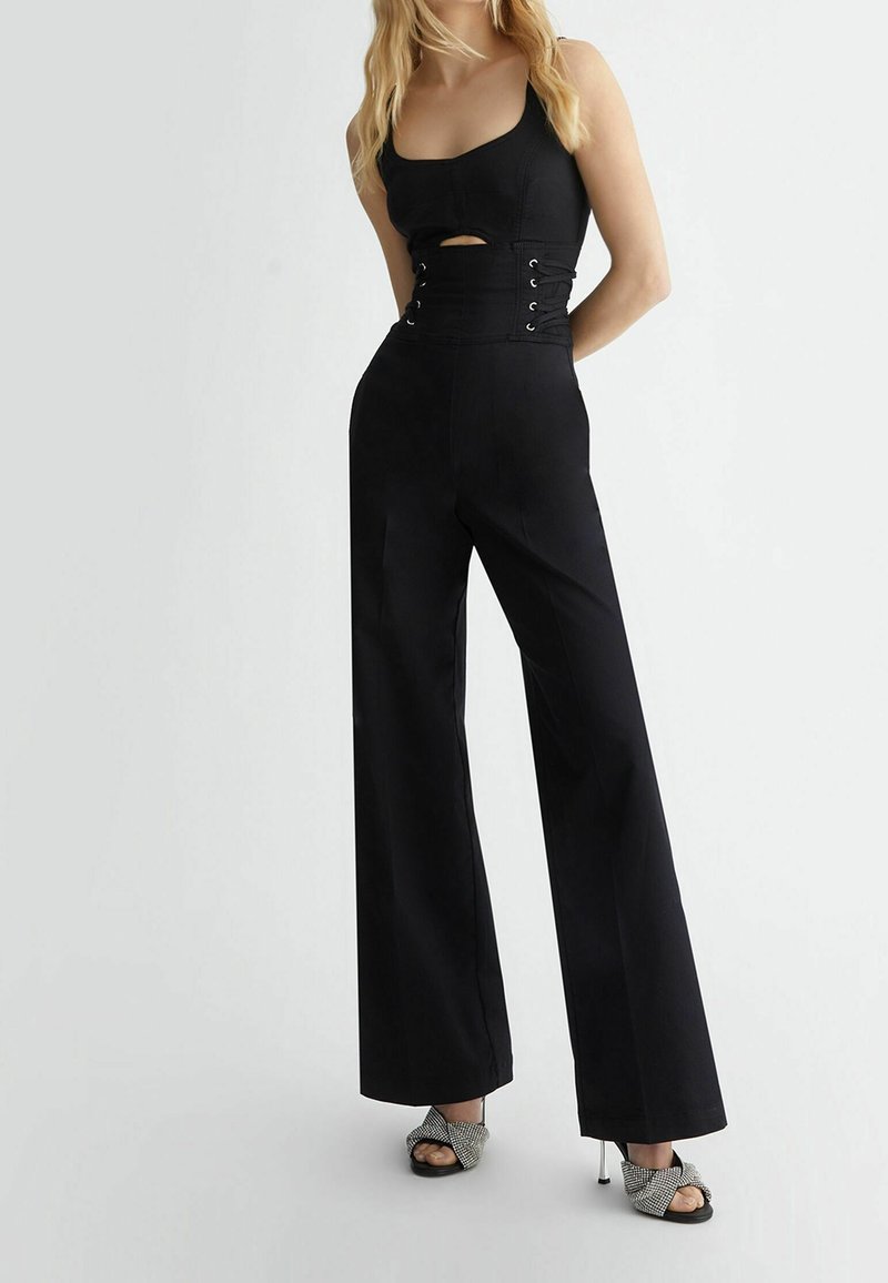 Top negro corto con un detalle de corte y pantalones negros de cintura alta. Los pantalones son de pierna ancha con una textura suave. El calzado presenta un diseño metálico.