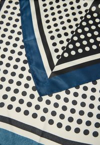 Zijde sjaal met een marineblauw en crèmekleurig kleurenschema, met grote zwarte stippen en geometrische patronen langs de randen. Glad textuur.