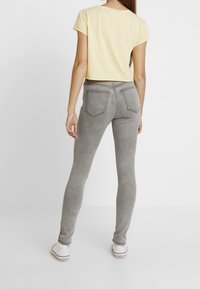 Jeans ajustados de mezclilla gris con bolsillos traseros y una textura suave, combinados con una camiseta amarilla de mangas cortas. Zapatillas blancas completan el conjunto.