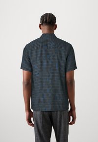 Camisa de manga corta de tela negra con un patrón de cuadros azules. Corte recto y cuello clásico, con un detalle de yugo único en la parte posterior.