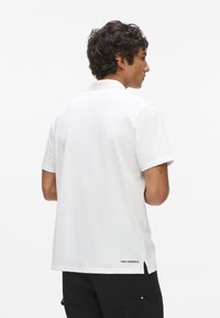 Fehér, rövid ujjú pólóing, pamutból készült, hímzett logóval az alján, és egyenes szabású dizájnnal.