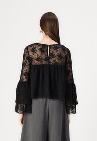Blusa nera in pizzo con maniche a sbuffo e apertura a chiave sulla schiena, caratterizzata da una sezione inferiore testurizzata e un motivo floreale in tutto.