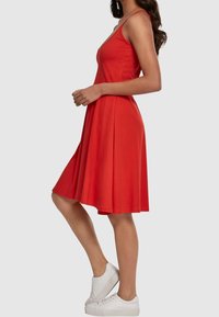 Robe sans manches rouge avec une jupe évasée, fabriquée en tissu doux. Présente un décolleté en V et tombe juste au-dessus du genou, associée à des baskets blanches.