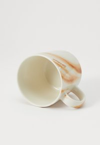 Keramický hrnček s okrúhlym tvarom, bielym základom a oranžovo-hnedým mramorovaním. Rukoväť na boku, naklonená tak, aby ukázala vnútro.