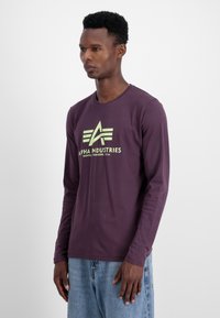 Dugi rukav ljubičasta majica s okruglim izrezom, s zelenim logotipom Alpha Industries na prsima i mekanim pamučnim materijalom.