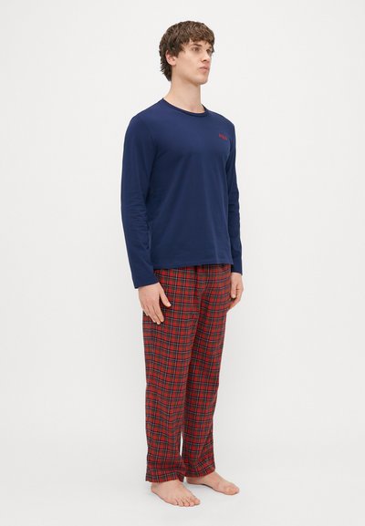 Camisa de manga longa azul-marinho com um logótipo vermelho, acompanhada por calças de pijama vermelhas em padrão xadrez. O conjunto apresenta um corte descontraído e uma textura de tecido suave.