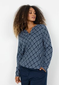 Tmavomodrá blúzka s geometrickým bielym vzorom, s výstrihom do V a dlhými rukávmi. Vyrobená z ľahkej, hladkej látky.