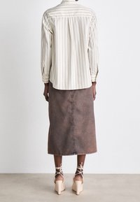 Stribet skjorte i lysecreme med lodrette linjer, parret med en knælængde brun denimnederdel og beige blokhælede sko.