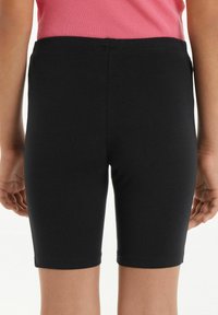 Shorts noirs en stretch avec une texture lisse, taille mi-haute et une coupe ajustée, arrivant au genou, vus de dos.