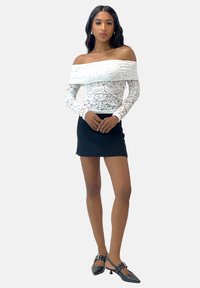 Bodysuit blanco de encaje sin hombros con mangas largas, combinado con una falda corta negra y zapatos negros con un pequeño tacón y detalle de hebilla.
