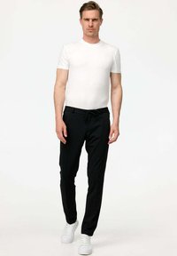 Pantaloni neri con vita elasticizzata abbinati a una t-shirt bianca aderente. I pantaloni presentano una texture liscia e un design a gamba dritta, completati da sneaker bianche.