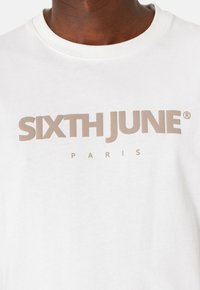 Hvid bomulds t-shirt med frontlogo-tryk i beige, der står "SIXTH JUNE PARIS," med rund hals og korte ærmer.