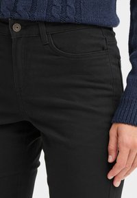 Black jeans made of soft, stretchy fabric, featuring a front pocket, button closure, and flat seams. The waistband is smooth with subtle stitching.