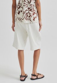 Biele ľanové šortky s voľným strihom, s nášivkami na švoch, skombinované s kvetinovým topom v zemských tónoch. Čierne sandále dopĺňajú outfit.