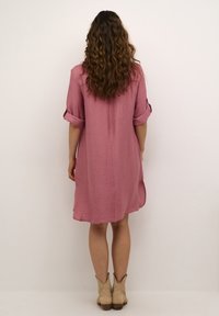 Vaaleanpunainen mekko, jossa on tekstuuri, lyhyet käärityt hihat ja löyhä malli, joka päättyy polven ylle. Yhdistetty vaaleisiin nilkkureihin.