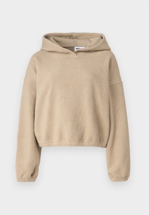 Beige bolyhos kapucnis pulóver, texturált felülettel, laza szabással, hosszú ujjakkal és zsinóros kapucnival. Rövidített hossza és elasztikus mandzsettái vannak.