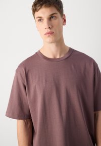 T-shirt de manga curta em mauve suave, com decote redondo e textura macia; ajuste descontraído com detalhes de costura mínimos.