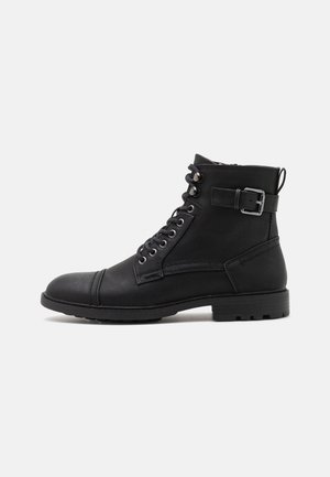 Bottines en cuir noir avec bout rond, lacets à l'avant, sangle à boucle ajustable et surface texturée avec une semelle robuste.