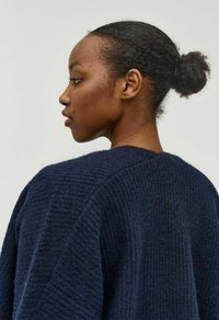 Jersey de punto azul marino con un patrón de textura y relieve; corte holgado; escote amplio y redondeado; mostrado en un modelo de perfil.