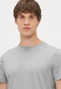 Pilkos spalvos medvilnės marškinėliai su apvaliu iškirpimu ir trumpomis rankovėmis, išsiskiriantys lygiu paviršiumi ir laisvu siluetu.