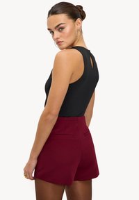 Body noir sans manches avec un dos ajouré associé à un short bordeaux taille haute avec deux poches arrière. Texture lisse.