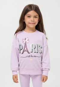 Liliowa bluza z grafiką błyszczącej wieży Eiffla, słowem "PARIS", kokardą i frazą "c'est la vie" w czarnym tekście. Miękka struktura.