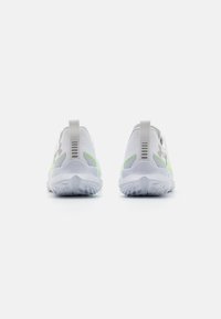 Scarpe sportive in mesh bianco con accenti verdi, dotate di linguette per il trasporto, suole testurizzate e un design aerodinamico per comfort e supporto.