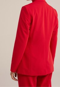 Röd skräddarsydd blazer med slim fit, mjuk textur och långa ärmar. Har strukturerade axlar och en ryggslits för rörlighet.