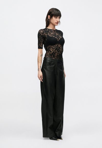 Fekete csipke felső rövid ujjakkal, testhez simuló anyag fölé rétegezve. Magas derekú, széles fekete bőr nadrággal párosítva.