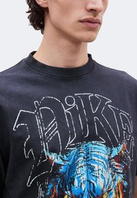 Νέος άνδρας φοράει μαύρο μπλουζάκι Nike με μεγάλο πολύχρωμο μπλε και κόκκινο γραφικό τύπωμα κεφαλιού ταύρου.