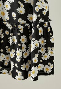Tessuto nero con un motivo di margherite bianche e gialle, con un orlo arricciato e dettagli di vita arricciata, che evidenziano un design floreale.