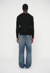 Čierny pletený sveter s dlhými rukávmi a okrúhlym výstrihom, skombinovaný so svetlomodrými, voľnými, mierne ošúchanými džínami a bielymi teniskami.