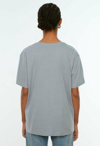 T-shirt grigia in cotone con una vestibilità rilassata, maniche corte e un ampio scollo rotondo, caratterizzata da una texture liscia e dettagli di cucitura minimi.