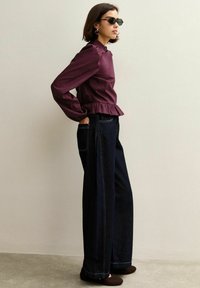 Bordeauxfärgad peplumblus med långa ärmar, tillsammans med vida mörkblå denimjeans med synliga sömmar och sidofickor. Svarta solglasögon.