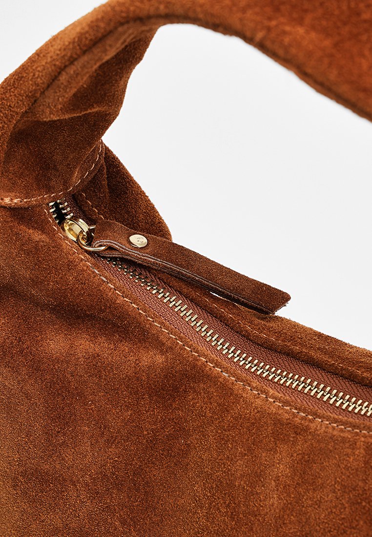 Braune Wildleder-Handtasche mit einem Reißverschluss, ausgestattet mit goldfarbenen Beschlägen und einer glatten Textur. Das Innere ist durch den offenen Reißverschluss sichtbar.