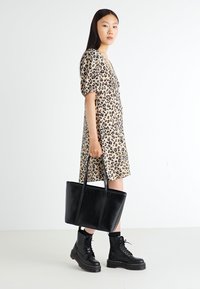 Leopardprint jurk met pofmouwen, gecombineerd met een zwarte leren tote bag en zwarte vetercombatboots, tegen een effen achtergrond.