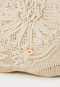 Bežna torba od čipke s složenim cvjetnim vezom, teksturiranim mrežastim uzorkom i malom metalnom oznakom u ružičastom zlatu s 'VB' logotipom.