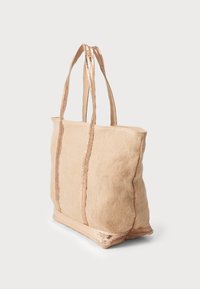 Šviesiai rudos spalvos tote krepšys su tekstūruota danga, išryškintais blizgiais metaliniais akcentais ant dirželių ir dugno, bei sustiprinta siūlėmis išilgai kraštų.