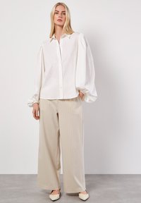 Camisa blanca de botones con mangas abullonadas, combinada con pantalones de pierna ancha beige con rayas. Tela suave con un corte relajado.
