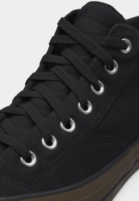 Mustade tossu paelte lähivaade, mis on sisse lükitud kuue hõbedase aasa kaudu musta pealiskihi külge, all on nähtav pruun tald.