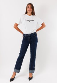 Maglietta bianca con stampa nera, jeans in denim blu, orli risvoltati e scarpe nere con tacco alto. Abbigliamento semplice e informale con linee pulite.