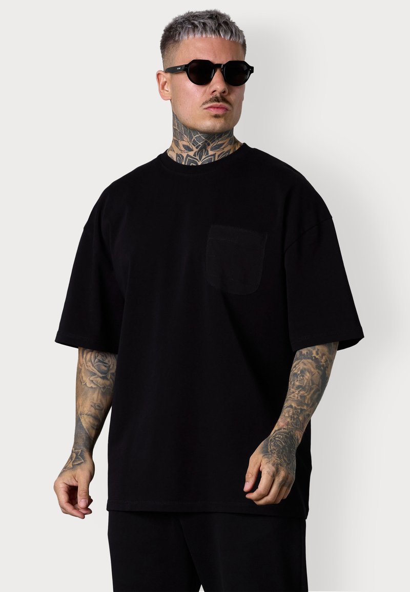 T-shirt en coton noir oversize avec un col rond et une poche poitrine gauche. Doté de manches courtes et d'une coupe ample, assorti à un pantalon noir.