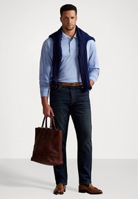 Lys blå polotrøye med marineblå genser drapert over skuldrene, mørke jeans, brun skinnbelte og brun skinnhandlenett. Brune sko.