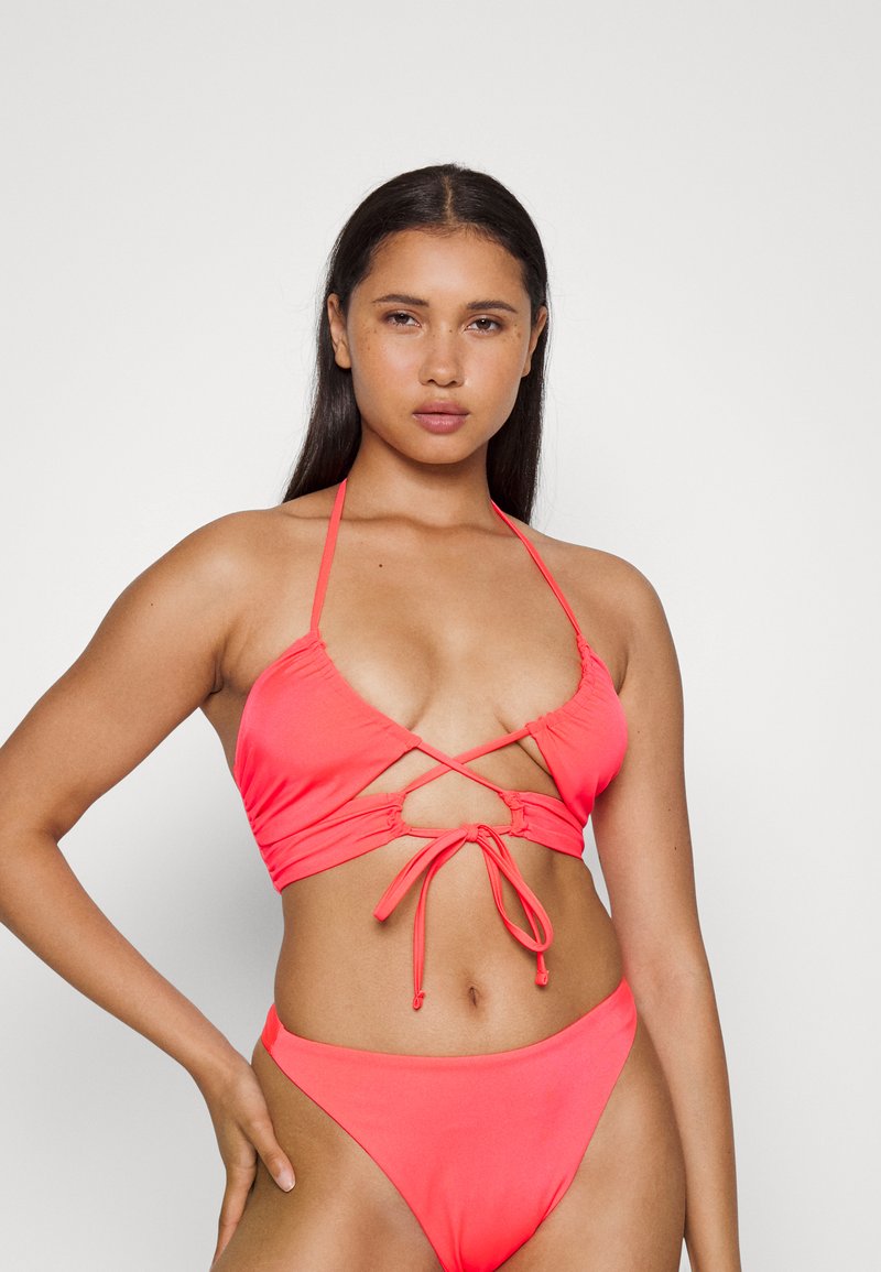 Conjunto de bikini cor-de-rosa com um top de halter com design entrelaçado e cordões ajustáveis, complementado por um fundo de cintura alta. Texture suave.